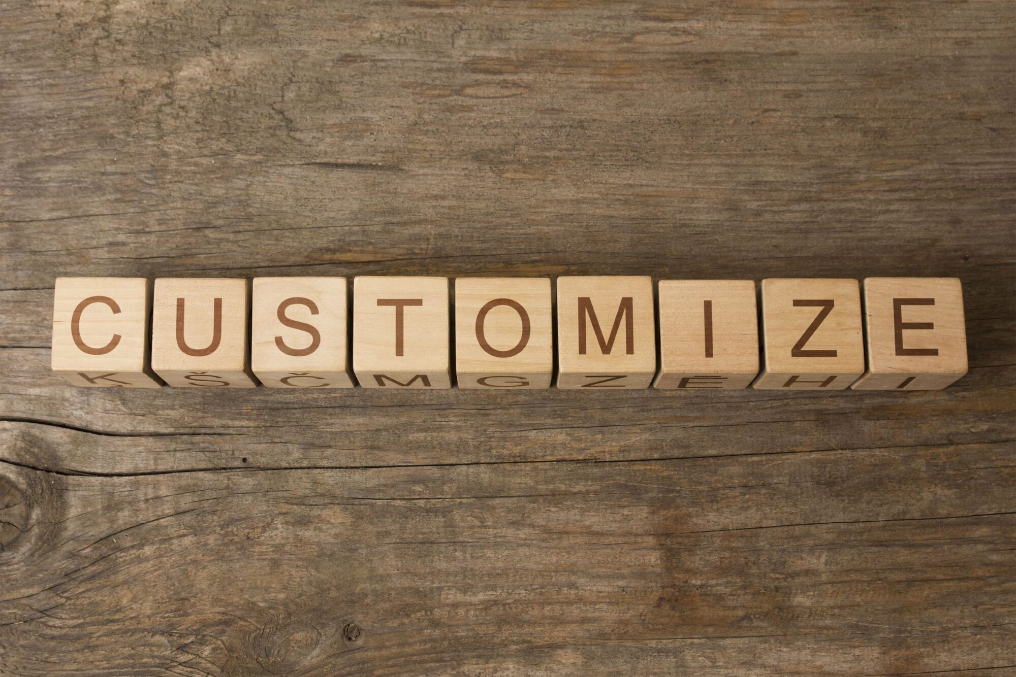 On a wood surface, 9 wood cubes spell the word CUSTOMIZE